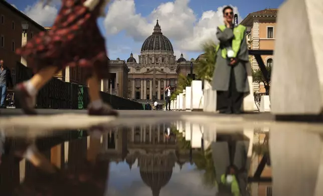People walk near the St. Peter's Basilica, background, in Rome, on Tuesday, May 6, 2025, the day before of the upcoming conclave starting on May 7, to elect the 267th Roman pontiff. (AP Photo/Francisco Seco)