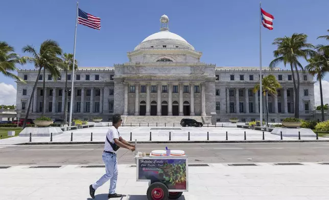 An ice cream vendor pushes his cart past Puerto Rico's Capitol building in San Juan, Puerto Rico, Thursday, May 8, 2025. (AP Photo/Alejandro Granadillo)