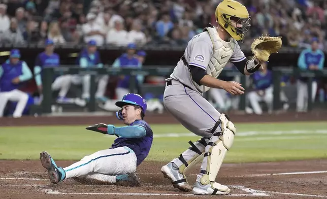 Arizona Diamondbacks' Corbin Carroll, left, scores a run as Colorado Rockies catcher Jacob Stallings waits for a late throw during the third inning of a baseball game Friday, May 16, 2025, in Phoenix. (AP Photo/Ross D. Franklin)