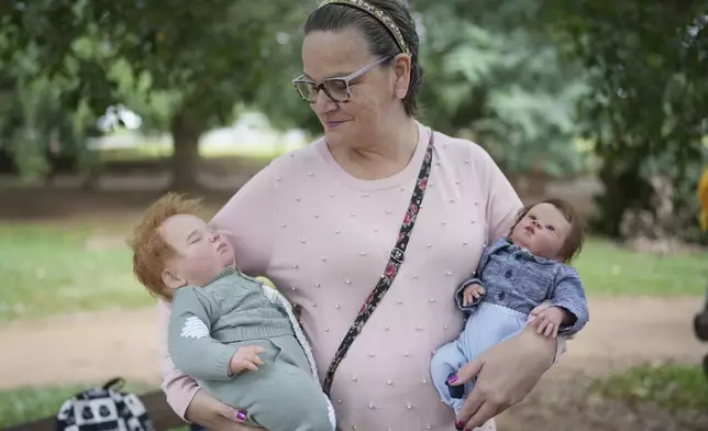 Ana Paula Vilela holds her dolls during a group gathering to bond and show off their hyper-realistic reborn baby dolls, in a park in Sao Paulo, Saturday, May 24, 2025. (AP Photo/Andre Penner)
