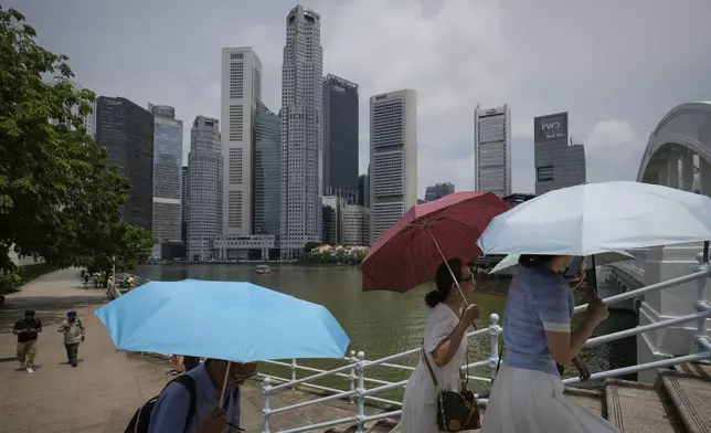 People walk with umbrellas, with the centre business district in the background, in Singapore, Friday, May 2, 2025. (AP Photo/Vincent Thian)