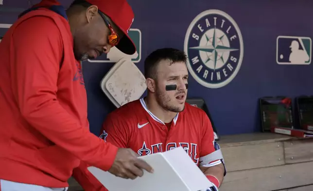 Los Angeles Angels' Mike Trout talks with batting coach Johnny Washington in the dugout before a baseball game against the Seattle Mariners, Wednesday, April 30, 2025, in Seattle. (AP Photo/John Froschauer)