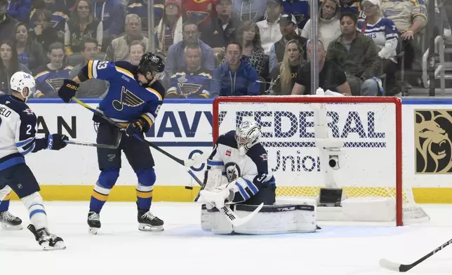 St. Louis Blues left wing Jake Neighbours (63) attempts a screen as Winnipeg Jets goaltender Connor Hellebuyck (37) makes a save during the first period in Game 6 of an NHL hockey first-round playoff series Friday, May 2, 2025, in St. Louis. (AP Photo/Jeff Le)