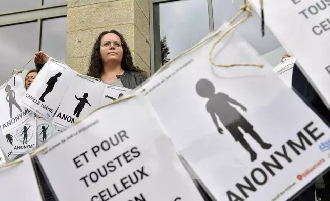 A woman peers behind a banner representing anonymous victims during a demonstration ahead of the verdict in the trial of Joel Le Scouarnec, a 74-year-old former surgeon, accused of raping and sexually assaulting 299 children, Wednesday, May 28, 2025 in Vannes, Brittany, western France. (AP Photo/Mathieu Pattier)