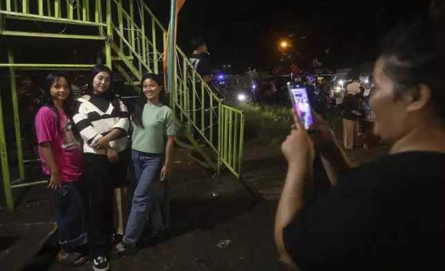Spectators take photos with 'wall of death' rider Sri Wahyuni, also known as Ayu, second left, at a fairground in Medan, North Sumatra, Indonesia, Saturday, May 10, 2025. (AP Photo/Binsar Bakkara)