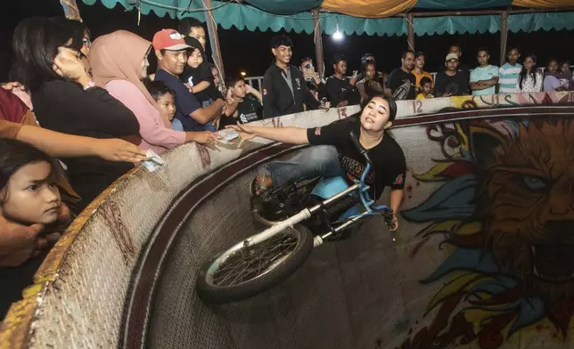 Sri Wahyuni, also known by her nickname Ayu, grabs tips from spectators as she rides a motorcycle in the "wall of death," locally known as "tong setan" or satan's barrel, at a fairground in Medan, North Sumatra, Indonesia, Sunday, May 11, 2025. (AP Photo/Binsar Bakkara)