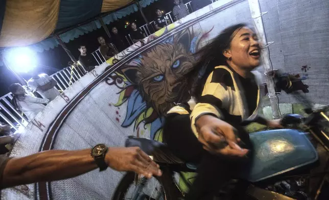 Sri Wahyuni, also known as Ayu, grabs tip from a spectator as she rides a motorcycle in the "wall of death", locally known as "tong setan" or satan's barrel, at a fairground in Medan, North Sumatra, Indonesia, Saturday, May 10, 2025. (AP Photo/Binsar Bakkara)