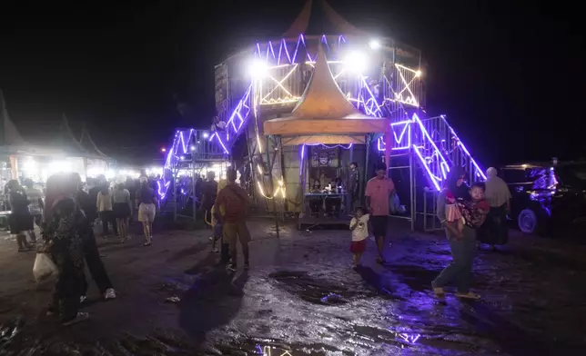 Sri Wahyuni, also known as Ayu, center, sits at the ticket desk before performing in a "wall of death," locally known as "tong setan" or satan's barrel, at a fairground in Medan, North Sumatra, Indonesia, Saturday, May 10, 2025. (AP Photo/Binsar Bakkara)
