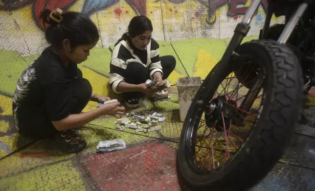Sri Wahyuni, also known by her nickname Ayu, left, and Rismauly Girsang, both "wall of death" riders, count tip money after a performance at a fairground in Medan, North Sumatra, Indonesia, Saturday, May 10, 2025. (AP Photo/Binsar Bakkara)