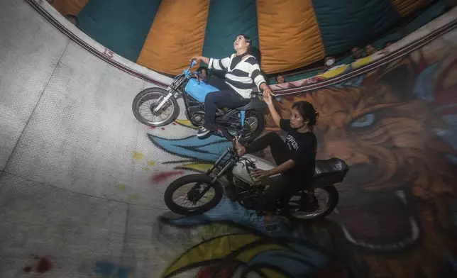 Sri Wahyuni, also known as Ayu, left, and Rismauly Girsang, perform in a "wall of death," locally known as "tong setan" or satan's barrel, at a fairground in Medan, North Sumatra, Indonesia, Saturday, May 10, 2025. (AP Photo/Binsar Bakkara)
