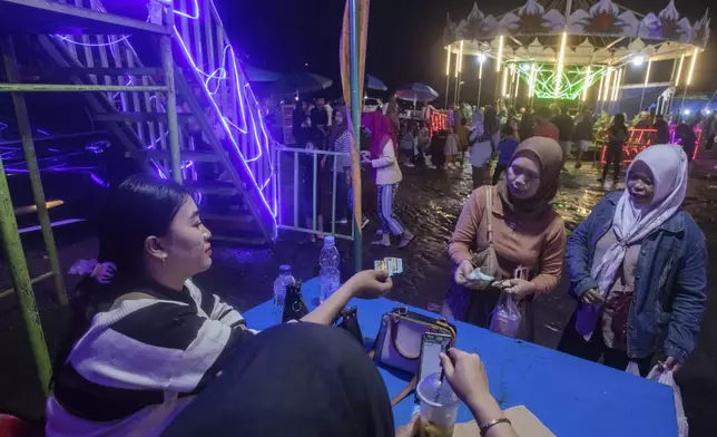 Sri Wahyuni, also known by her nickname Ayu, left, hands out tickets to spectators before performing in a "wall of death" at a fairground in Medan, North Sumatra, Indonesia, Saturday, May 10, 2025. (AP Photo/Binsar Bakkara)