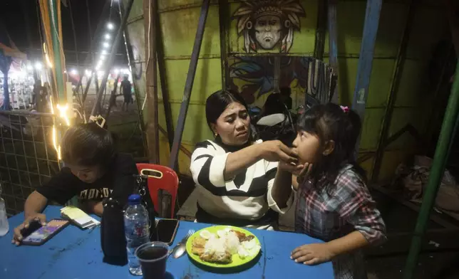 Sri Wahyuni, also known by her nickname Ayu, a "wall of death" rider, feeds her daughter Aqilla, in between performances at a fairground in Medan, North Sumatra, Indonesia, Saturday, May 10, 2025. (AP Photo/Binsar Bakkara)
