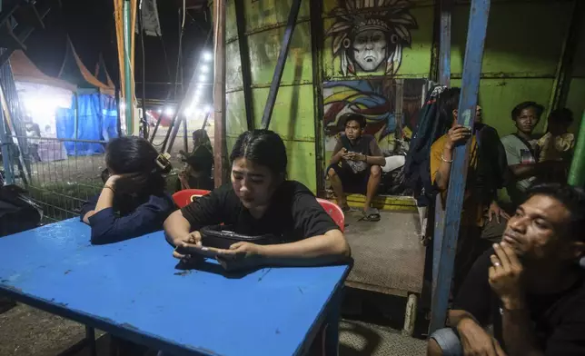 Sri Wahyuni, who is also known as Ayu, center, and Rismauly Girsang, left, take a break with their crew after performing in a "wall of death," locally known as "tong setan" or satan's barrel, at a fairground in Medan, North Sumatra, Indonesia, Friday, May 9, 2025. (AP Photo/Binsar Bakkara)