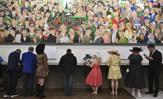 People stand against a wall at Churchill Downs before the 151st running of the Kentucky Derby horse race Saturday, May 3, 2025, in Louisville, Ky. (AP Photo/Jon Cherry)