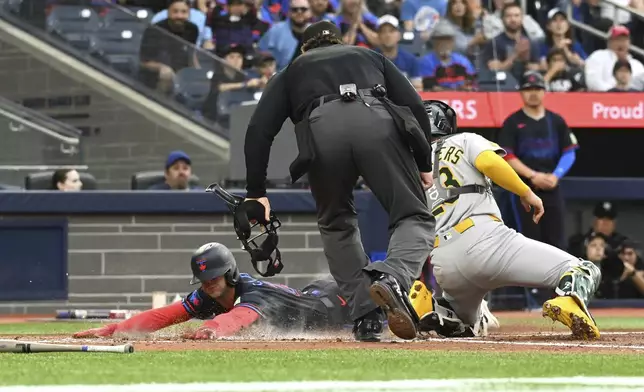 Toronto Blue Jays' Ernie Clement (22) slides safely into home ahead of a tag by Athletics catcher Shea Langeliers (23) in second inning MLB baseball action in Toronto on Friday, May 30, 2025. (Jon Blacker/The Canadian Press via AP)