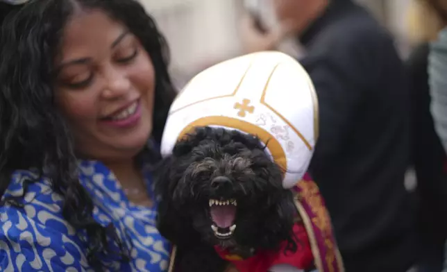 Meryl Espiniero from New York holds her dog Romeo Valentino at St. Peter's square where people wait to see smoke pour from the chimney of the Sistine Chapel where 133 cardinals are gathering on the second day of the conclave to elect a successor to late Pope Francis, at the Vatican, Thursday, May 8, 2025. (AP Photo/Andrew Medichini)