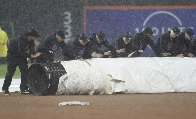 Grounds crew members cover the field as it rains during the third inning of a baseball game between the New York Mets and the Los Angeles Dodgers, Friday, May 23, 2025, in New York. (AP Photo/Pamela Smith)