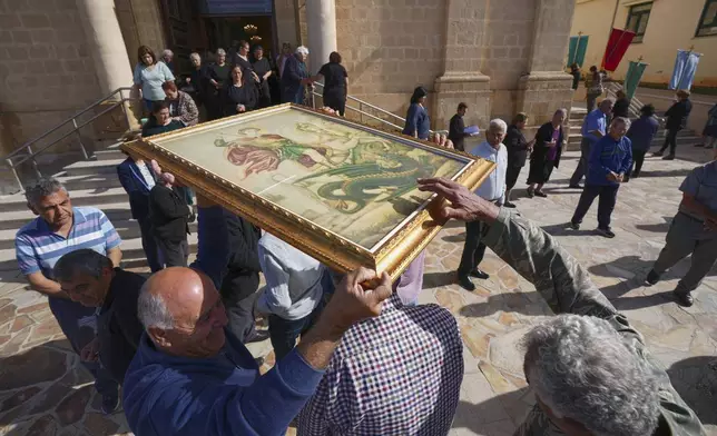 Catholic Maronite faithful pass under the icon of St. George in an act of supplication during a traditional procession on the saint's Feast Day outside St. George Church in the Maronite village of Kormakitis in the breakaway north of the ethnically divided Cyprus on Wednesday, April 23, 2025. (AP Photo/Petros Karadjias)