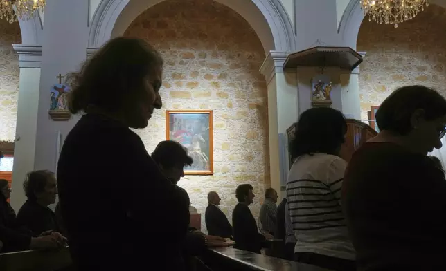 Maronite Catholic faithful are silhouetted against the sunlit wall of St. George Church in the Maronite village of Kormakitis in the breakaway north of the ethnically divided Cyprus on Wednesday, April 23, 2025. (AP Photo/Petros Karadjias)