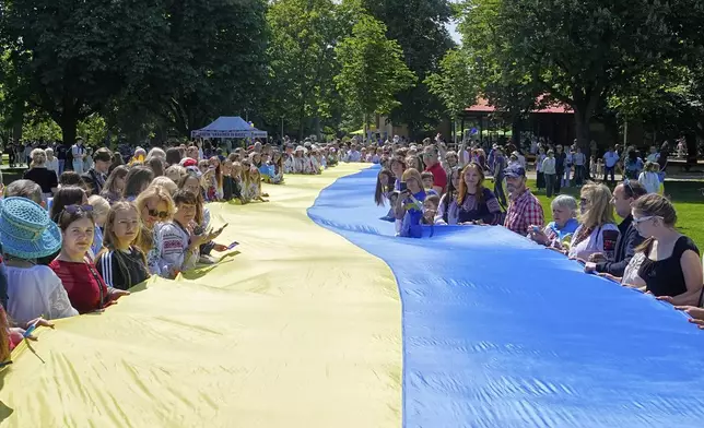 People from Ukraine hold a giant Ukrainian flag during a family meeting with their Eurovision band Ziferblat in a park in Basel as part of the 69th Eurovision Song Contest week, in Basel, Switzerland, Thursday, May 15, 2025. (AP Photo/Martin Meissner)