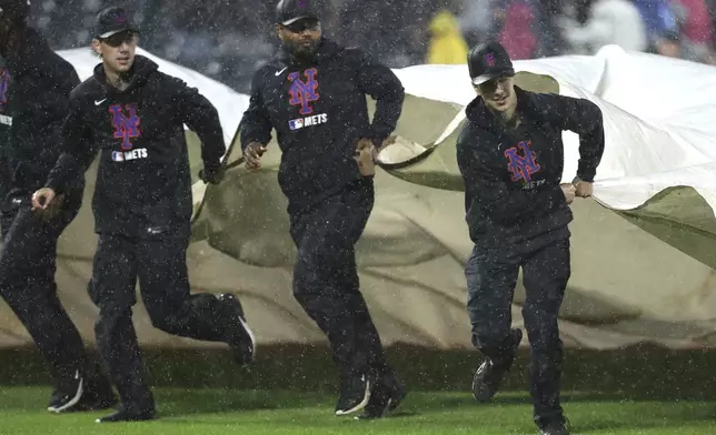 Grounds crew members cover the field during the third inning of a baseball game between the New York Mets and the Los Angeles Dodgers, Friday, May 23, 2025, in New York. (AP Photo/Pamela Smith)