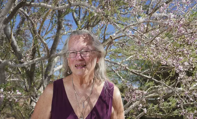 Linda Hilton, a 76-year-old retired office worker, stands in front of her favorite tree in front of her home Tuesday, May 13, 2025, in Apache Junction, Ariz. (AP Photo/Ross D. Franklin)