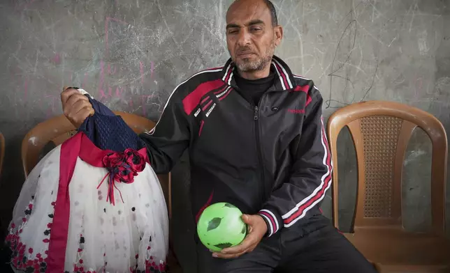 Samy Abed shows a dress Tuesday, April 29, 2025, that his 4-year-old daughter, Massa, wore for the Eid festivities and a ball she used to play with before she was killed by an Israeli army strike in Zawaida, near the city of Deir al-Balah, Gaza Strip. (AP Photo/Abdel Kareem Hana)