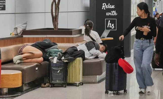 A traveler passes sleeping passengers at Newark Liberty International Airport, in New Jersey, Friday, May 23, 2025. (AP Photo/Richard Drew)
