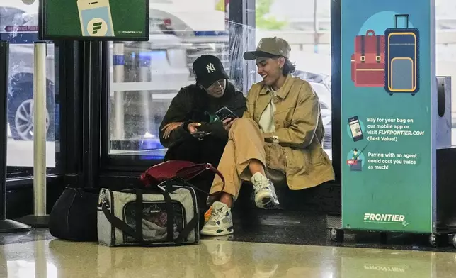 Passengers consult their mobile phones at Newark Liberty International Airport, in New Jersey, Friday, May 23, 2025. (AP Photo/Richard Drew)