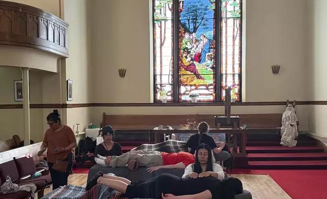 Guadalupe Gonzalez, foreground center, and two other practitioners perform Reiki treatments in the sanctuary of St. Paul’s-San Pablo Lutheran Church, where congregant Lizete Vega, left, helped organize wellness sessions as part of its migrant ministry, in Minneapolis, Sunday, April 27, 2025. (AP Photo/Giovanna Dell’Orto)
