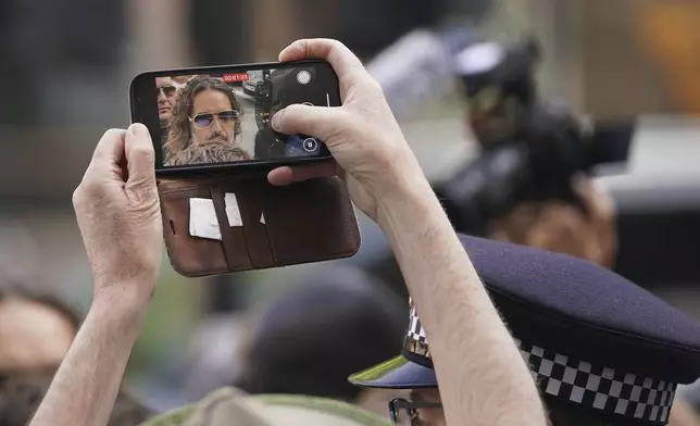 A person takes a smart phone picture as Russell Brand arrives at Westminster Magistrates' court in London, Friday, May 2, 2025, where he faces, rape and sexual assault charges involving four women. (AP Photo/Alberto Pezzali)