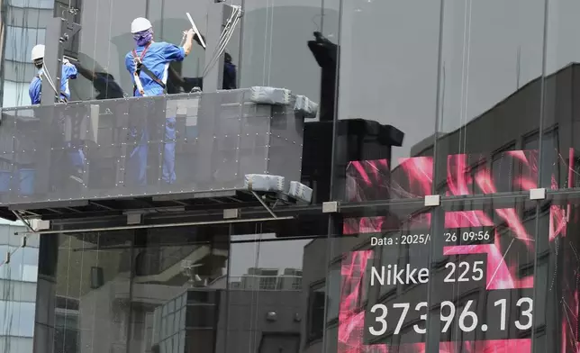 Workers clean the glass window of a building in front of an electronic stock board showing Japan's Nikkei index at a securities firm Monday, May 26, 2025, in Tokyo. (AP Photo/Eugene Hoshiko)