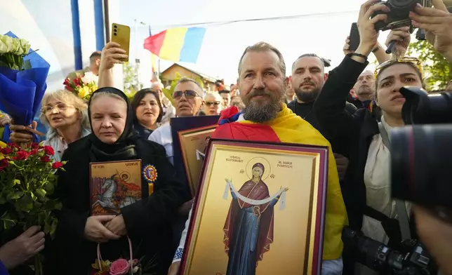 Supporters hold religious icons outside the voting station where Calin Georgescu, winner of the first round of last year's annulled election, and Presidential candidate George Simion voted in the first round of the presidential election redo in Bucharest, Romania, Sunday, May 4, 2025. (AP Photo/Vadim Ghirda)