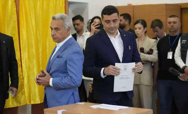 Presidential candidate George Simion, right, casts his vote next to Calin Georgescu, winner of the first round of last year's annulled election, during the first round of the presidential election redo in Bucharest, Romania, Sunday, May 4, 2025. (AP Photo/Vadim Ghirda)
