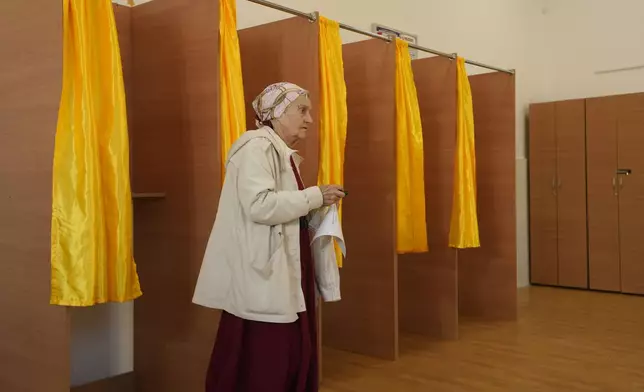 A woman exits a voting booth before casting her vote in the first round of the presidential election redo in Bucharest, Romania, Sunday, May 4, 2025. (AP Photo/Vadim Ghirda)
