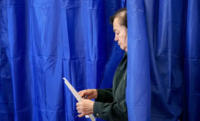 A woman exits a voting booth before casting her vote in the first round of the presidential election redo in Bucharest, Romania, Sunday, May 4, 2025. (AP Photo/Andreea Alexandru)