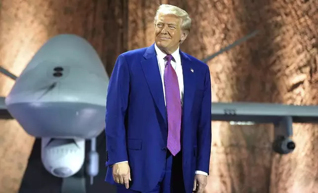 President Donald Trump smiles backdropped by an MQ-9 Reaper drone before addressing military personnel at the Al Udeid Air Base, Thursday, May 15, 2025, in Doha, Qatar. (AP Photo/Alex Brandon)