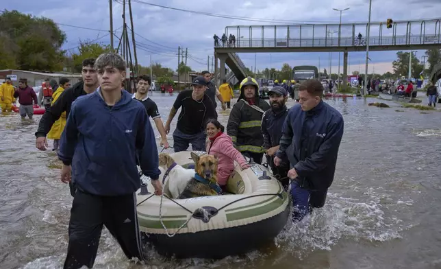 Residents and rescue workers evcuate a woman and dogs on an inflatable boat, through a flooded street following heavy rains in Campana, Argentina, Saturday, May 17, 2025. (AP Photo/Rodrigo Abd)