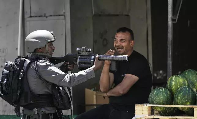An Israeli border police officer takes up position next to a watermelon vendor, during a military raid in the Askar refugee camp near the West Bank city of Nablus, Tuesday, May 20, 2025. (AP Photo/Majdi Muhammad)