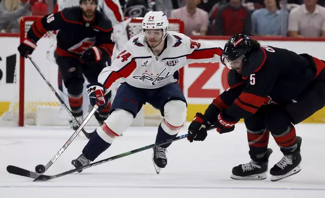 Washington Capitals' Connor McMichael (24) tries to chip the puck past Carolina Hurricanes' Jalen Chatfield (5) during the first period of Game 3 of an NHL hockey Semi-final round playoff series in Raleigh, N.C., Saturday, May 10, 2025. (AP Photo/Karl DeBlaker)