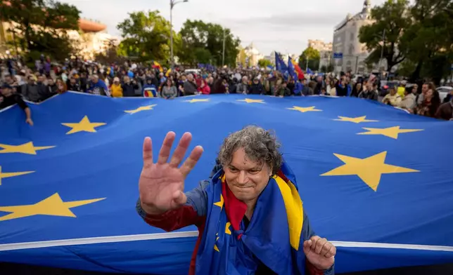A man with Romanian and European Union flags draped over his shoulders waves in front of a large EU flag, during a pro-EU rally ahead of the second round of the presidential election redo in Bucharest, Romania, Friday, May 9, 2025. (AP Photo/Andreea Alexandru)