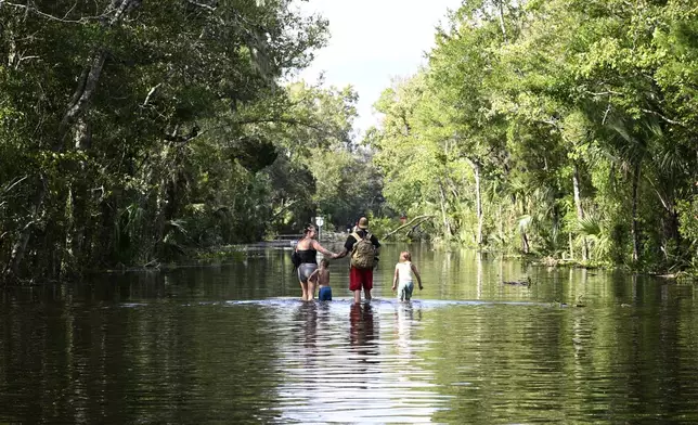 FILE - Dustin Holmes, second from right, holds hands with his girlfriend, Hailey Morgan, while returning to their flooded home with her children Aria Skye Hall, 7, right, and Kyle Ross, 4, in the aftermath of Hurricane Helene, Sept. 27, 2024, in Crystal River, Fla. (AP Photo/Phelan M. Ebenhack, File)
