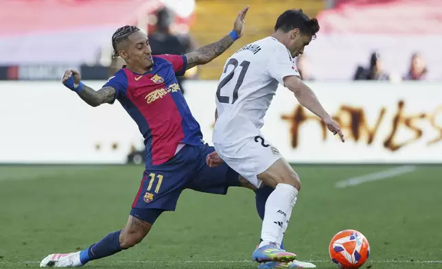 Barcelona's Raphinha tackles Real Madrid's Brahim Diaz during the La Liga soccer match between Barcelona and Real Madrid in Barcelona, Spain, Sunday, May 11, 2025. AP Photo/Joan Monfort)