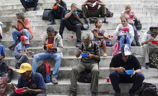 People eat soup donated by the Christ on the Street Christian church, in Caracas, Venezuela, Sunday, April 20, 2025.(AP Photo/Cristian Hernandez)