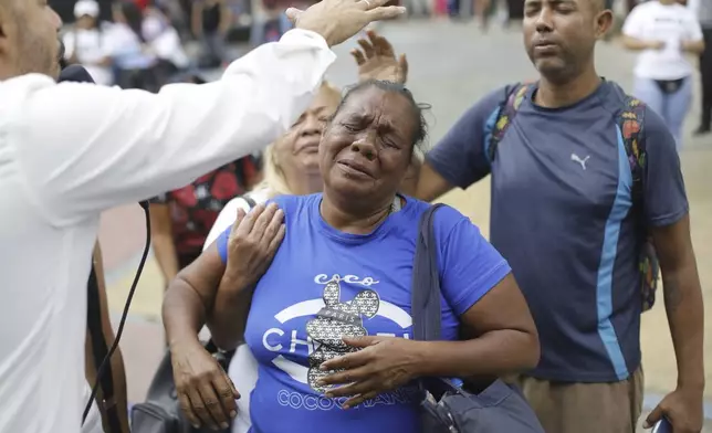 Pastor Siro Salazar, left, prays over congregant with a laying of hands during a service in a downtown square of Caracas, Venezuela, Saturday, April 5, 2025. (AP Photo/Cristian Hernandez)