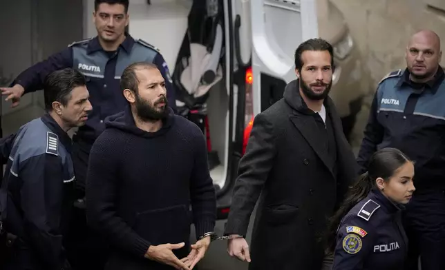FILE- Police officers escort Andrew Tate, center, handcuffed to his brother Tristan Tate, to the Court of Appeal in Bucharest, Romania, Monday, Feb. 27, 2023. (AP Photo/Andreea Alexandru, File)