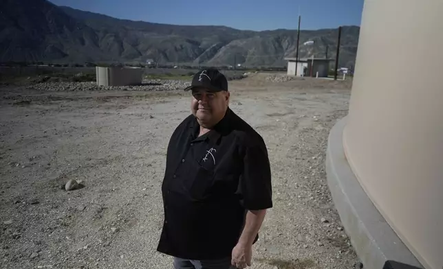 Mark Whaling, a retired firefighter, stands in front of a Heli-Hydrant, a small, open tank that helicopters can rely on to get water faster for urban fires, Friday, April 11, 2025, in Cabazon, Calif. (AP Photo/Brittany Peterson)