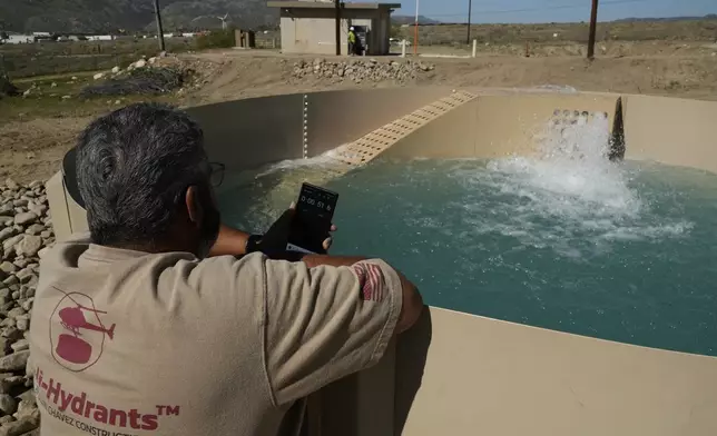 Glenn Chavez sets a timer as water fills a newly installed Heli-Hydrant, a small, open tank that helicopters can rely on to get water faster for urban fires, Friday, April 11, 2025, in Cabazon, Calif. (AP Photo/Brittany Peterson)