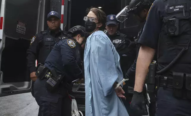 A person wearing graduate robes is detained by police across the street from the main gates of Columbia University, Wednesday, May 21, 2025, in New York. (AP Photo/Heather Khalifa)