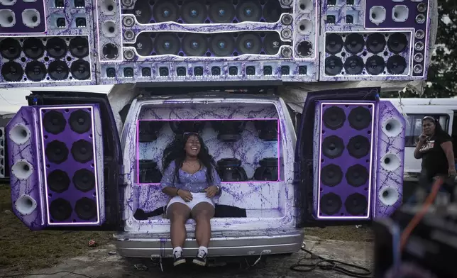 A woman sits on speakers playing music during a Red Devils bus exhibition in La Chorrera, Panama, Sunday, June 30, 2024. (AP Photo/Matias Delacroix)